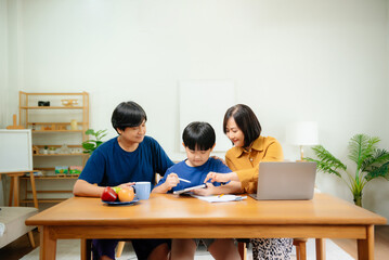 Homeschool Asian young little boy learning online and does homework by using computer and tablet with mother help, teach and encourage.
