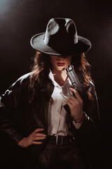 Fototapeta premium portrait of a female detective in a coat and hat with a gun in her hands. A book drama noir portrait in the style of detectives of the 1950s.