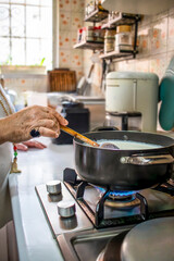 Senior woman cooking milk in a saucepan on the stove