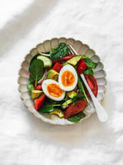 Delicious breakfast, snack - boiled egg, fresh vegetable salad on a light background, top view
