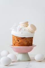 Easter cake decorated with white icing and macaroons. Traditional sweet Easter bread on the stand surrounded with colorful painted eggs on white background. Copy space