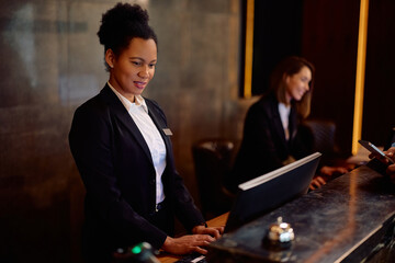 Black female receptionist working on computer at hotel front desk.