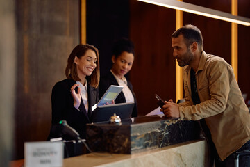 Happy female receptionist using touchpad while welcoming guest in hotel.