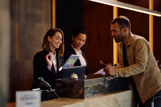 Happy female receptionist using touchpad while welcoming guest in hotel.