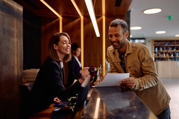 Happy female receptionist assisting guest with filling out documents in hotel.