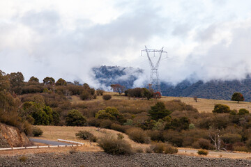 Metal powerpole with power lines going to it through mist and low cloud