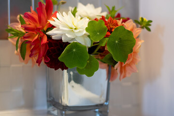 Multi-colored dahlias and orange nasturtiums in a mirror vase.