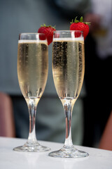 Two champagne flutes with strawberries on rim, filled with bubbl