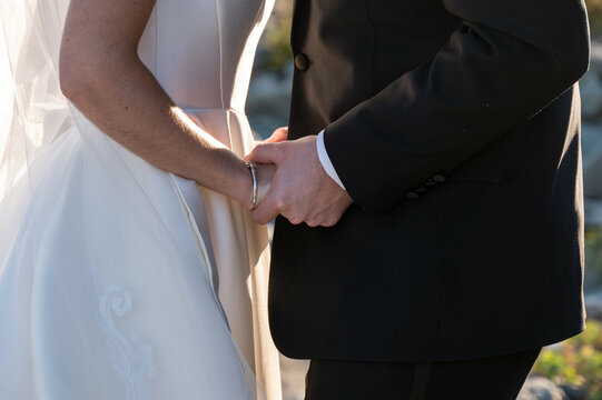 Bride and groom holding hands in sunlight during wedding ceremon