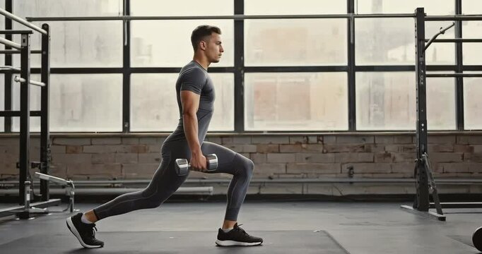 Man Doing Lunges with Dumbbells: A strong, fit man performs a dumbbell lunge exercise in a modern gym. The image focuses on strength training and fitness.