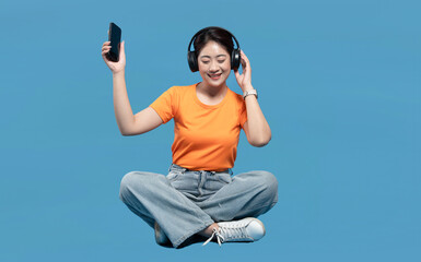 Happy young woman in casual wear listening to music on headphones and holding a smartphone