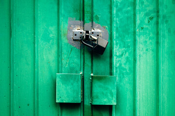 Old green worn metallic garage door with padlock as grunge background and texture