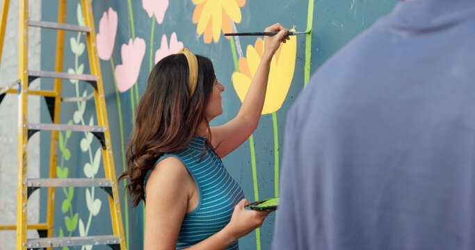 Woman, creative and painting in city for wall art, mural process or project to uplift community. People, team creativity or outdoor with paintbrush for floral design, volunteer collaboration or hobby