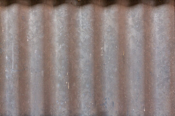 A close-up reveals the textured, rusty metal surface of an old, corrugated iron sheet, its gray and silver lines forming a grunge pattern