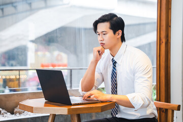 Thoughtful professional at cafe working on his laptop near a bright window thinking deeply
