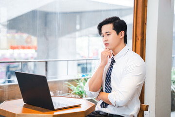 Thoughtful professional working on a laptop in a modern office setting with a window view