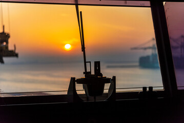 Gyro compass repeater silhouette on the cargo ship navigational bridge. Ship equipment seen against sunrise in the port.
