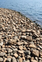 Rough quay, brown stones scattered amongst pebbles, coastal waterfront scene, rough surface, gravel, earth tones