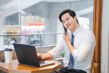Business professional working remotely engaged in a phone call while using a laptop in a cafe