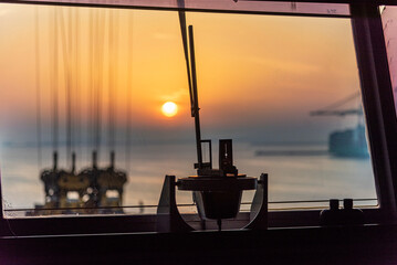 Gyro compass repeater silhouette on the cargo ship navigational bridge. Ship equipment seen against sunrise in the port.