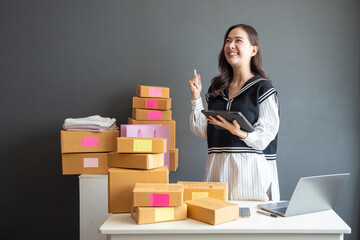 Startup successful small business owner. Woman using smartphone or digital tablet taking receive and checking online purchase shopping order to preparing a package box to deliver to customers. Selling
