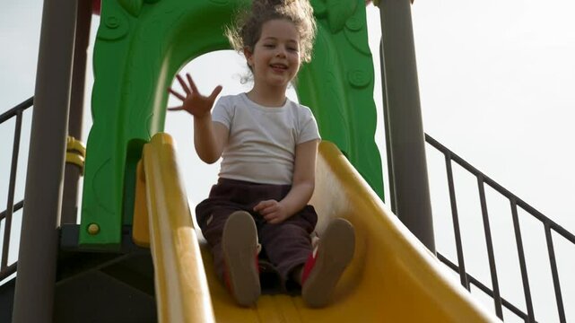 A cheerful toddler slides down a yellow slide at a playground, looking happy and enjoying the ride