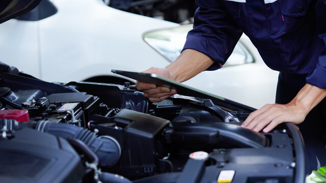 Mechanic in work gloves repairs car engine in auto repair shop. Auto mechanic checks vehicle with wrench, fixes issues. Car service, maintenance, engine diagnostic, automotive repair.