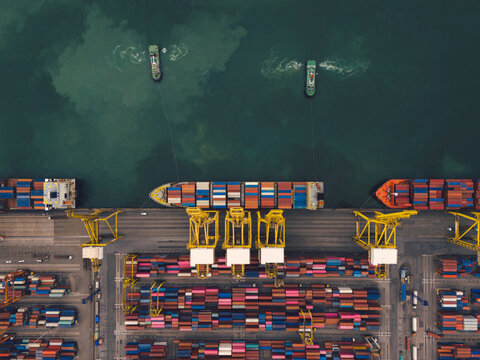 Aerial top view over international containers cargo ship at industrial import-export port prepare to load containers with big container loader ship vessel. global transportation and logistic business.