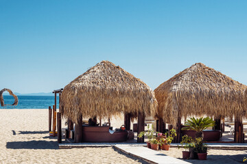 Weekend at sea. Relaxing summer day at the beach with sunbeds and a shaded area by the sea. Thatched gazebo on the beach
