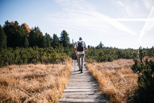 Older man hiking wooden trail through South Tyrol meadow