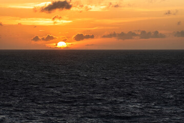 A serene sunset over the Indian Ocean with calm, dark waters below and a red sky painted with soft clouds above. A mesmerizing, tranquil moment that captures the beauty of the evening.