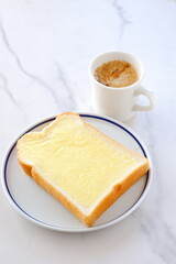 マーガリンを塗った厚切りパンと、淹れたてで香りのよいコーヒーで、朝食のイメージ
