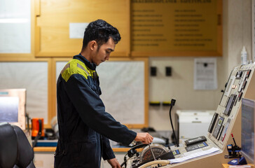 The marine engineer officer stands at the main engine control station in the engine control room,...