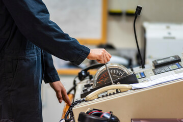 The hand of an operator grips the engine telegraph lever in the engine control room of a merchant ship, ready to issue commands to control the main engine's speed.