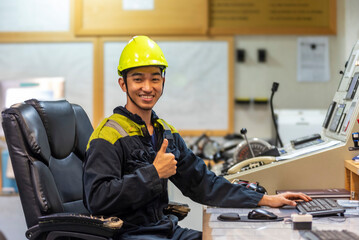 The marine engineer officer sits in the control room of a merchant vessel, focused on recording key...