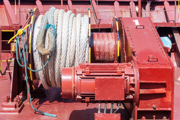 Close-up of a large mooring winch on the bow of a cargo ship, painted red and showing details of the heavy-duty maritime equipment used during berthing operations.