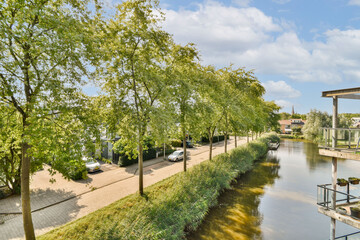 A picturesque scene showcasing a tranquil river bordered by vibrant trees, complemented by a well-maintained pathway and modern architecture in the background.