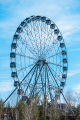 Fototapeta premium Ferris wheel standing tall against a blue sky, with trees and rocky terrain in the foreground, creating a picturesque scene