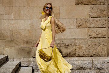 Summer fashion model in flowing yellow maxi dress poses in the city on a sunny summer day.