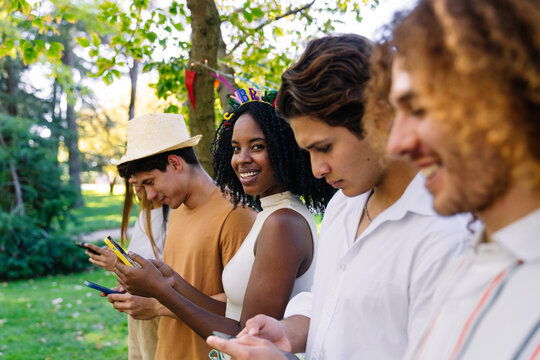 Group of diverse friends using their smartphones at an outdoor birthday party, enjoying social media and communication