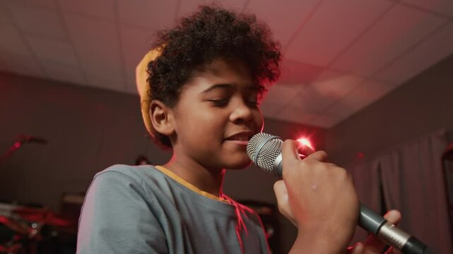 Low angle view of African American adolescent boy vocalist singing into microphone with closed eyes in professional studio