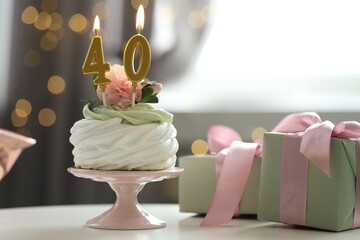 40th birthday. Tasty cupcake with burning number shaped candles and gift boxes on table against blurred background with lights, bokeh effect