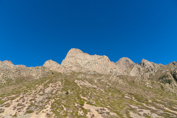 Kabardino-Balkaria. El-Tyubu. Rocky mountains with trees growing on their slopes glow in morning sun. Close-up. Chegem Gorge. Unique rocky ridge with steep cliffs against blue autumn sky.