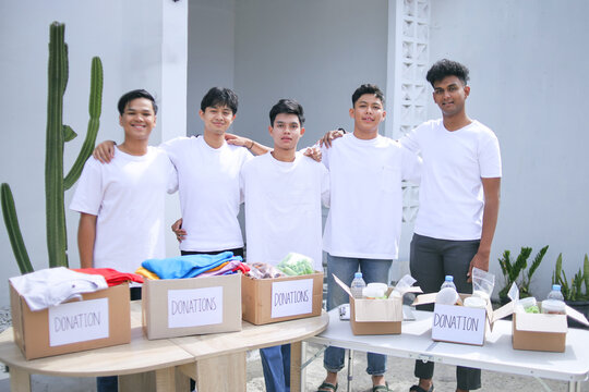 Diverse Multinational Team Of Young Volunteers Standing Together In Row With Boxes On Table