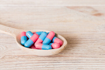 Vitamin capsules in a spoon on a colored background. Pills served as a healthy meal. Red soft gel...