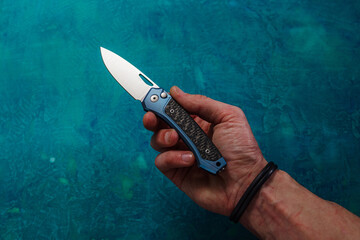 A man holds a knife in his hand. A folding knife lying in his hand. A knife on a man's palm. An outstretched hand with a knife.