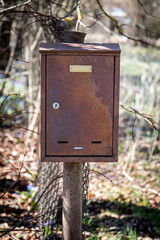 Rusty Mailbox on Pole in Outdoor Area with Trees in Background