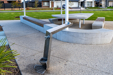 a water fountain near a modern seating area in a residential neighborhood park with tables. Public commintiy emnities in parkland of a suburb of australia.