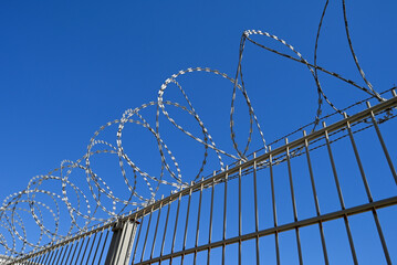 Clôture avec du fil barbelé enroulé dessus sur fond de ciel bleu © Richard Villalon