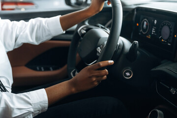 Two hands are on the steering wheel. Woman in white shirt is in the modern car